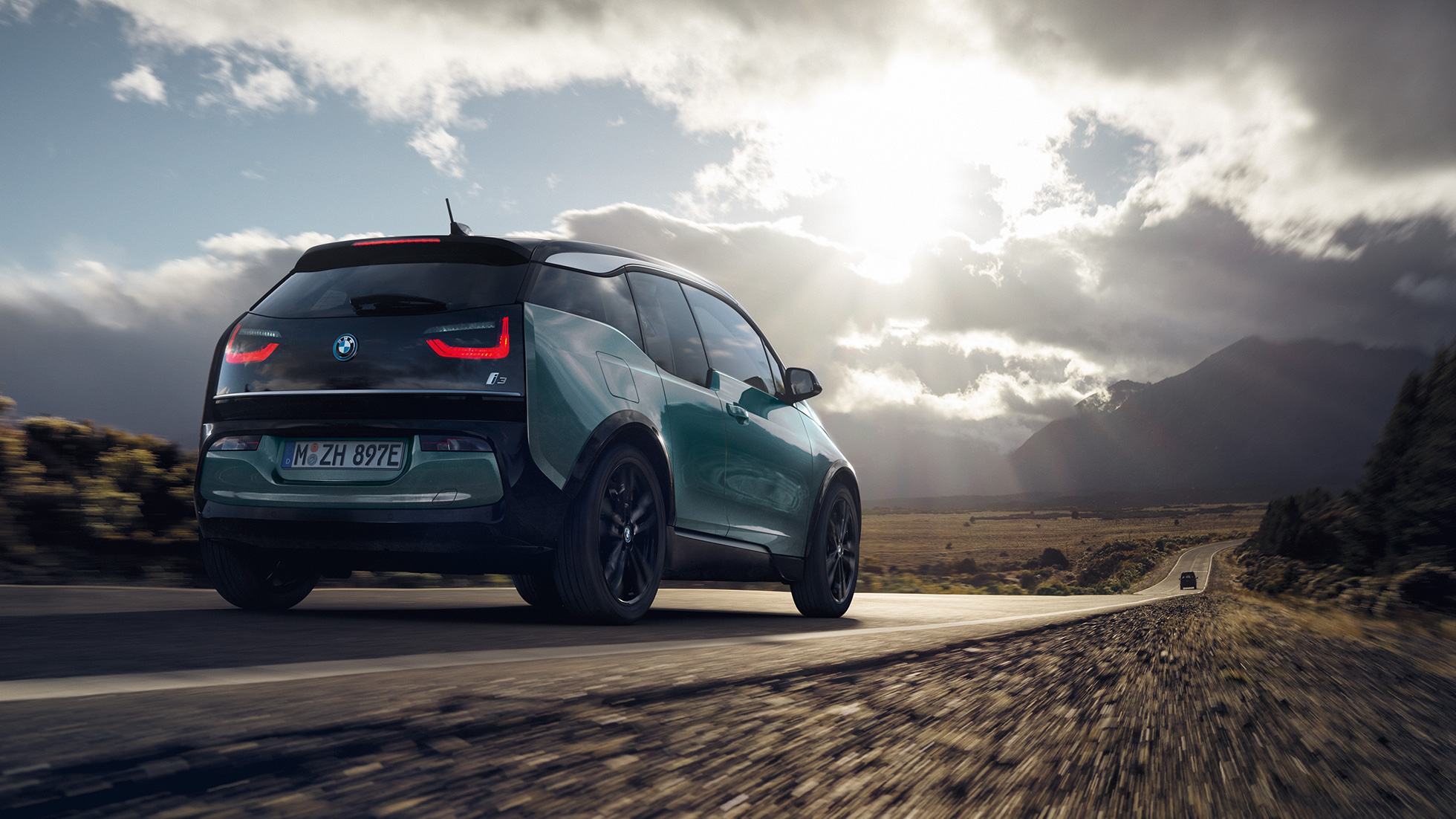BMW i3 2018 í akstri á þjóðvegi, skásett sjónarhorn á afturhluta BMW i3 I01 2018, Jucaro-drapplitaður með frostgráum sanseruðum áherslulit, skásett sjónarhorn á afturhluta í akstri á þjóðvegi
