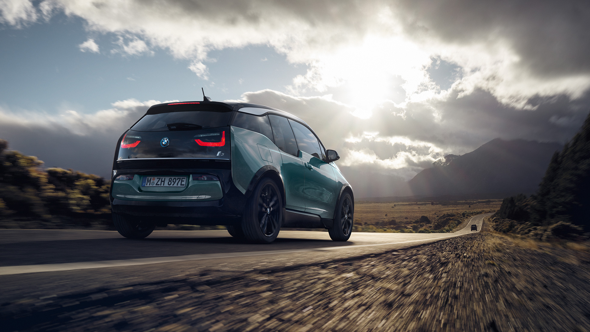BMW i3 2018 í akstri á þjóðvegi, skásett sjónarhorn á afturhluta BMW i3 I01 2018, Jucaro-drapplitaður með frostgráum sanseruðum áherslulit, skásett sjónarhorn á afturhluta í akstri á þjóðvegi
