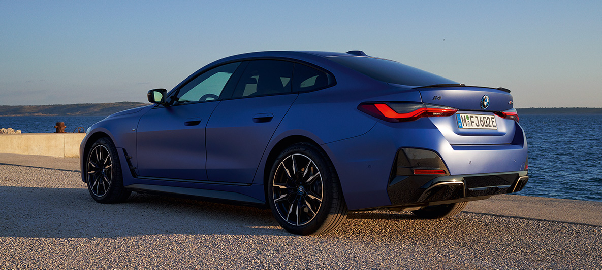 BMW i4 M50 G26 2021, skásett sjónarhorn á afturhluta BMW i4 M50 G26 2021 M Portimao Blue metallic þriggja fjórðu aftar útsýni í fjörunni