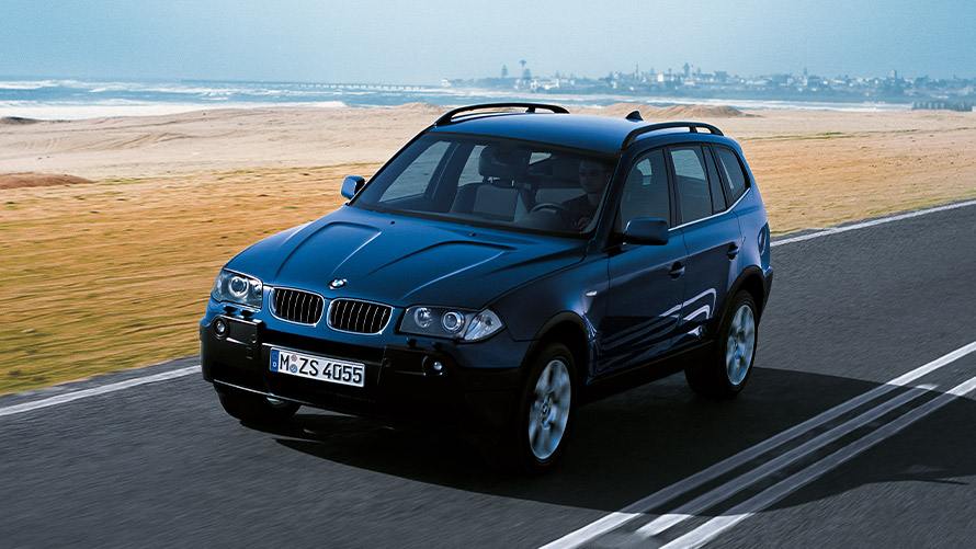 Fyrsta kynslóð BMW X3 E83 ekur á götu, skásett sjónarhorn á framhluta BMW X-línan – fyrsta kynslóð BMW X3 E83 ekur á götu, skásett sjónarhorn á framhluta