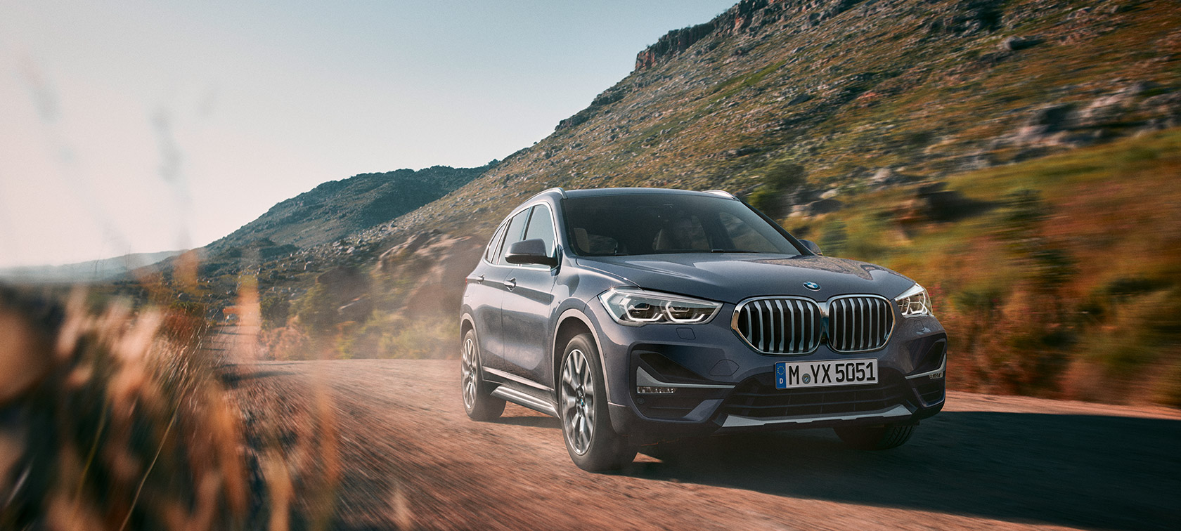 BMW X1, three-quarter front view driving in front of mountain scenery.