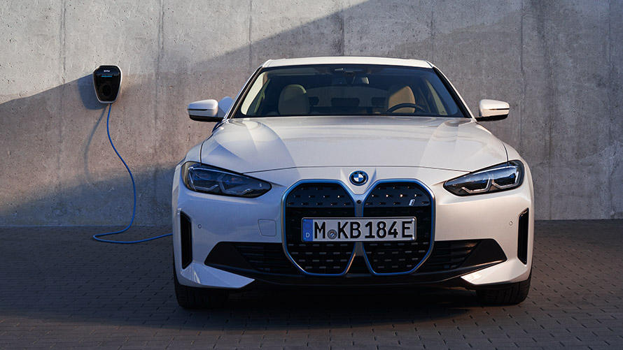 BMW iX xDrive50 i20, skásett sjónarhorn á afturhluta Skásett sjónarhorn á afturhluta BMW iX xDrive50 i20 í bílageymslu við hlið innstungu og festingar fyrir hleðslusnúru