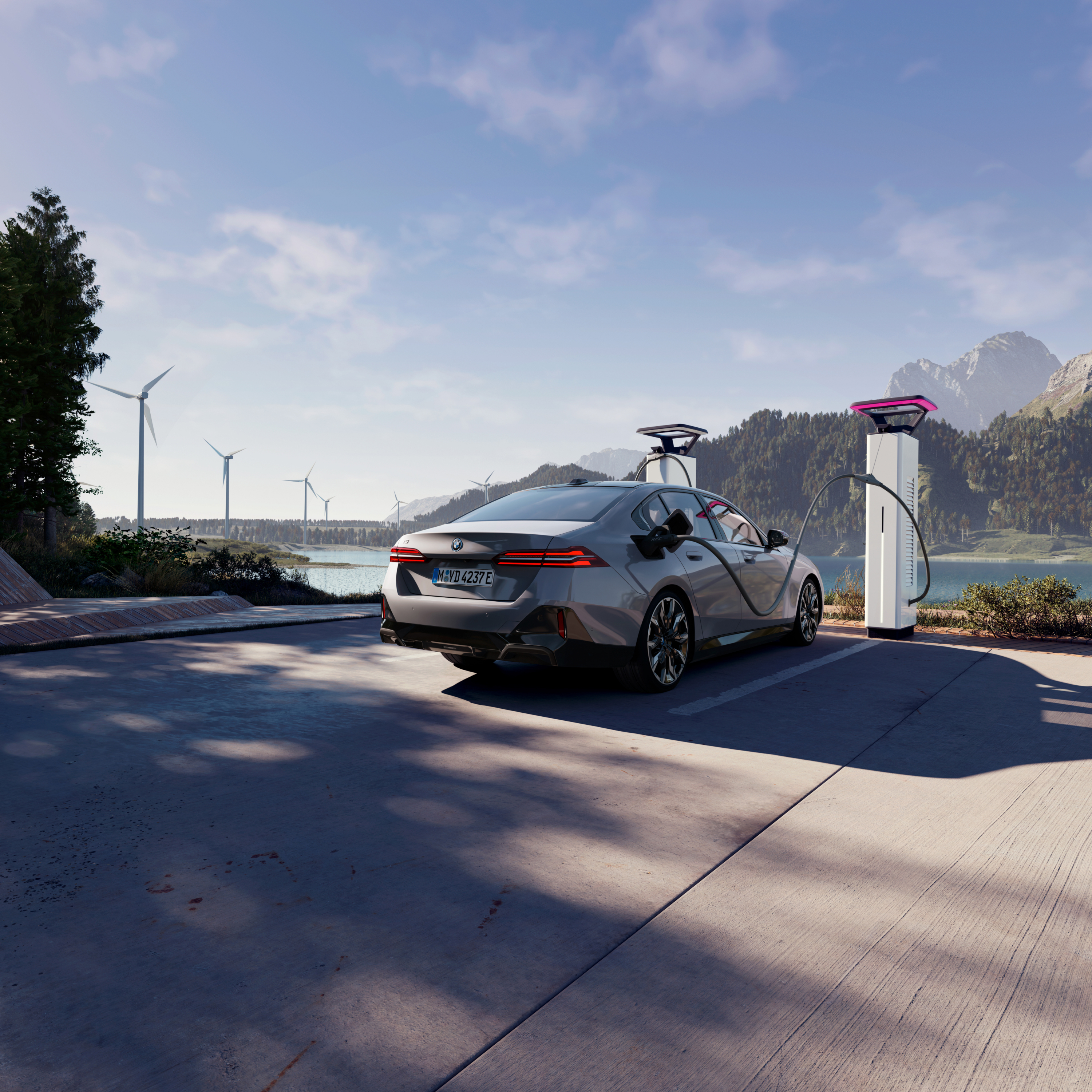 BMW í hleðslu við hleðslupóst með útsýni yfir vatn, fjöll og vindmyllur